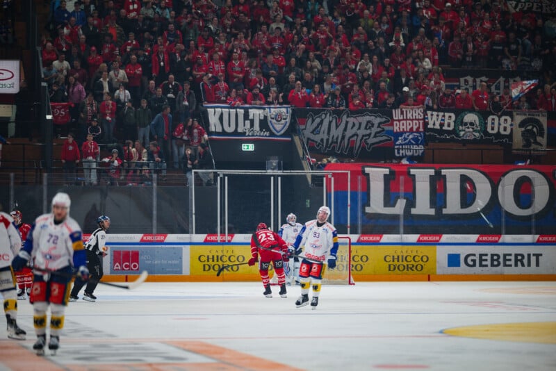 Jugadores de hockey sobre hielo durante el partido, con una gran multitud de aficionados vestidos de rojo y sosteniendo pancartas al fondo. El ambiente era animado y animado.