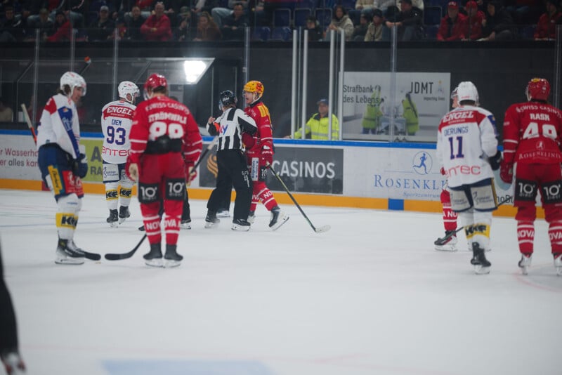 Durante los partidos, los jugadores de hockey con uniformes rojos y blancos se reúnen en el hielo, con los árbitros parados cerca del centro. Los espectadores se sentaron en las gradas detrás de un cristal protector.