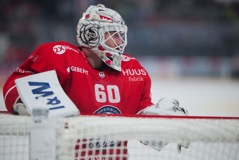 Durante el partido, el portero de hockey sobre hielo con la camiseta roja número 60, con un casco blanco y grandes guantes protectores, permaneció vigilante frente a la red. El fondo se vuelve borroso y la atención se centra en el jugador.