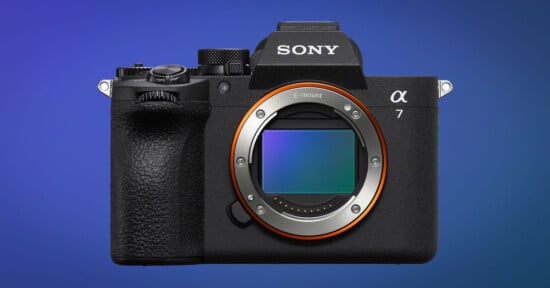 A Sony Alpha 7 mirrorless digital camera body is shown facing forward, displaying its large sensor and lens mount, against a blue gradient background.