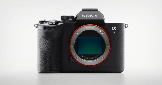 A Sony Alpha 7 mirrorless digital camera body is shown facing forward on a plain white background, with the lens removed to reveal the camera's image sensor.