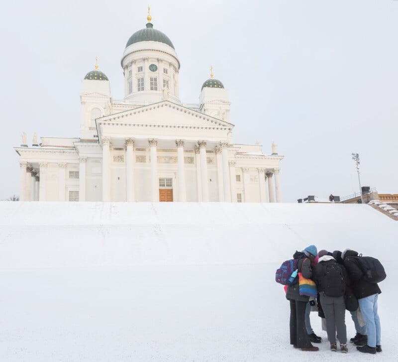 Cinco personas con mochilas se apiñaban frente a la catedral de Helsinki cubierta de nieve, un gran edificio blanco con una cúpula verde y adornos dorados.