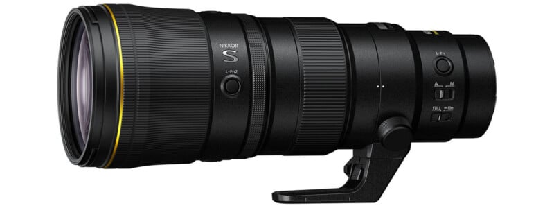 A large, professional Nikon NIKKOR camera lens with a tripod mount, control buttons, and a gold ring near the front element, shown against a white background.