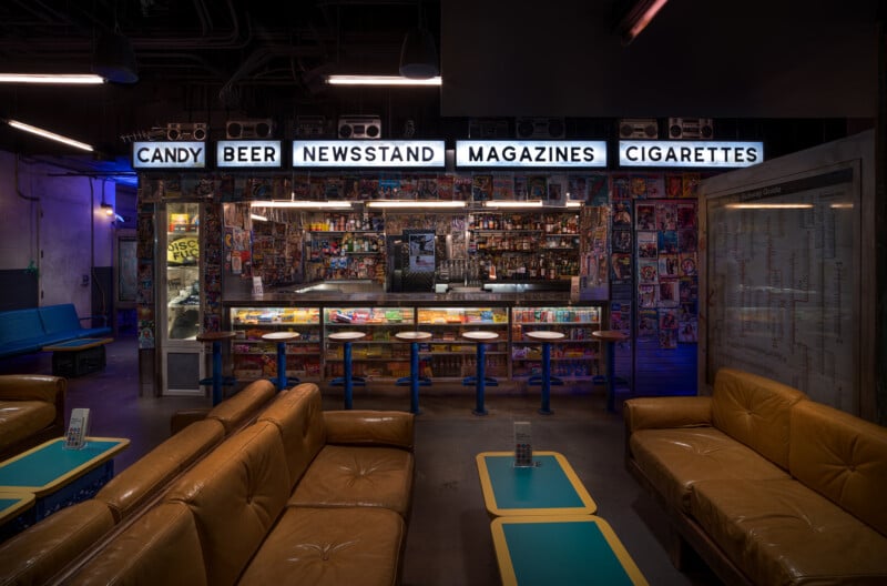 Zona de bar de estilo retro con sofás de cuero marrón, mesas azules y taburetes de bar. En lo alto, los carteles de neón decían