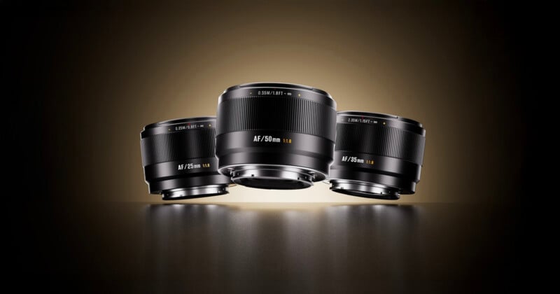 Three camera lenses labeled AF 24mm, AF 50mm, and AF 85mm are displayed on a dark reflective surface with a warm gradient background, positioned upright with the 50mm lens in the center.