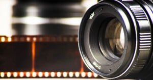 Close-up of a camera lens with a blurred film strip in the background, evoking a sense of photography and analog film.