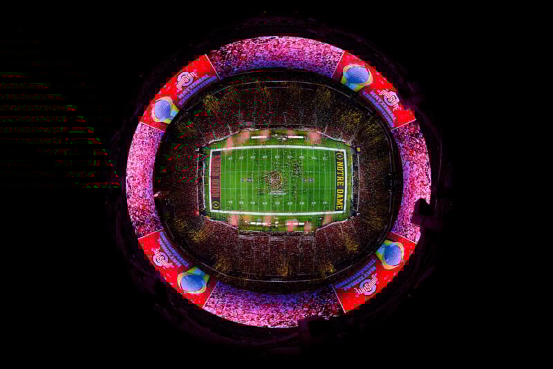 Aerial, circular fisheye view of a brightly lit football stadium filled with fans, with the green field at the center and vibrant pink and red lights illuminating the stands. Ohio State Buckeyes logos are visible on big screens.