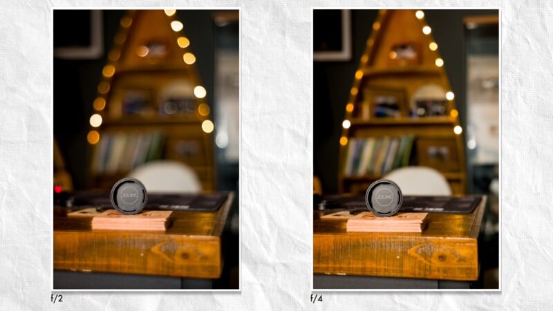 Side-by-side photos comparing a camera lens on a wooden table, with the left image (f/2) showing a blurred background and the right image (f/4) showing a sharper background with more details visible.