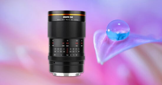 A camera lens with detailed markings stands against a soft, colorful background featuring a close-up of a petal with a water droplet.