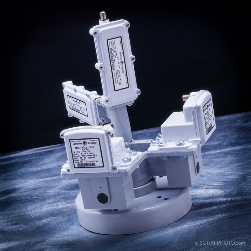 A mechanical device with a round white base and multiple jointed arms, each fitted with rectangular labeled modules, positioned on a textured blue-grey surface.