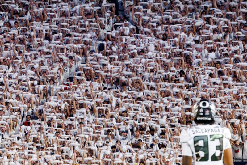 A football player on the field faces a large stadium crowd dressed in white, waving white towels in unison, creating a sea of white in the stands.