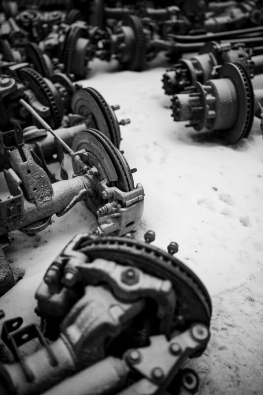 La fotografía en blanco y negro muestra varios ejes y cubos de ruedas desmontados, dispuestos en hileras sobre el suelo nevado, con engranajes y componentes de freno visibles.