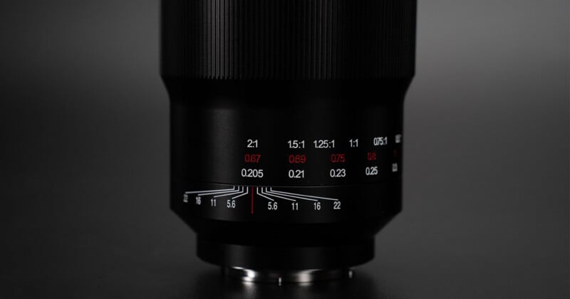 Primer plano de la lente de la cámara negra con marcas blancas y rojas que indican la apertura y se centran en un fondo oscuro. La montura del objetivo y el grabado detallado son claramente visibles.