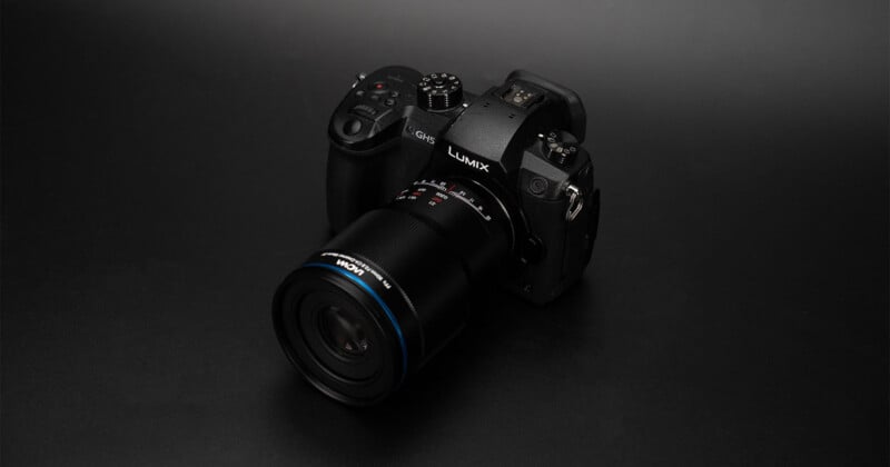 Cámara Panasonic Lumix negra con lente grande colocada sobre una superficie mate oscura con fondo neutro.