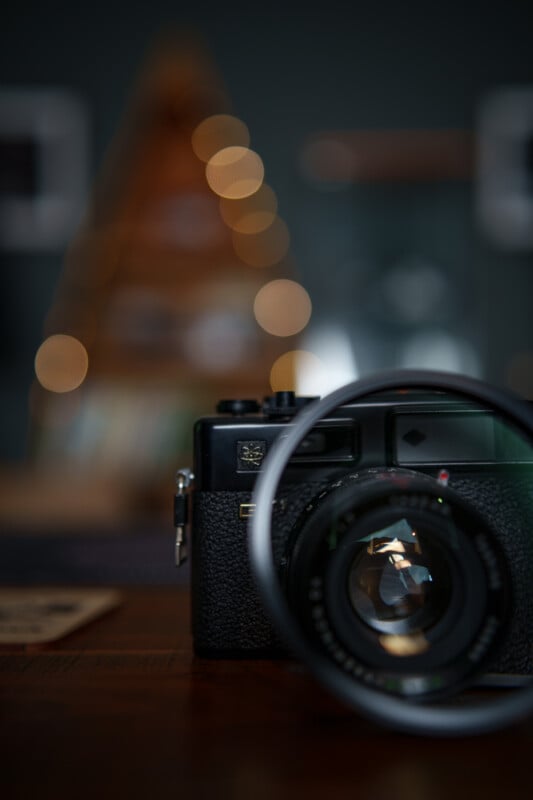 Una cámara vintage negra con lente grande se asienta sobre una superficie de madera con un fondo borroso con cálidas luces bokeh redondas y formas borrosas.