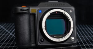A close-up of a Hasselblad digital camera body, showing the lens mount and sensor. The camera sits on a grid-patterned surface with a black background.