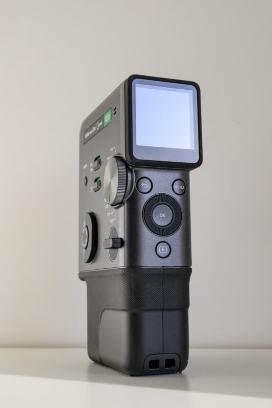 A close-up of a black, handheld electronic device with a display screen, multiple buttons, and dials, standing upright against a plain, light-colored background.