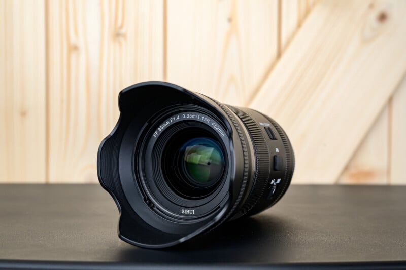 Lente de cámara gran angular con parasol colocado sobre una superficie negra con paneles diagonales sobre fondo de madera clara.