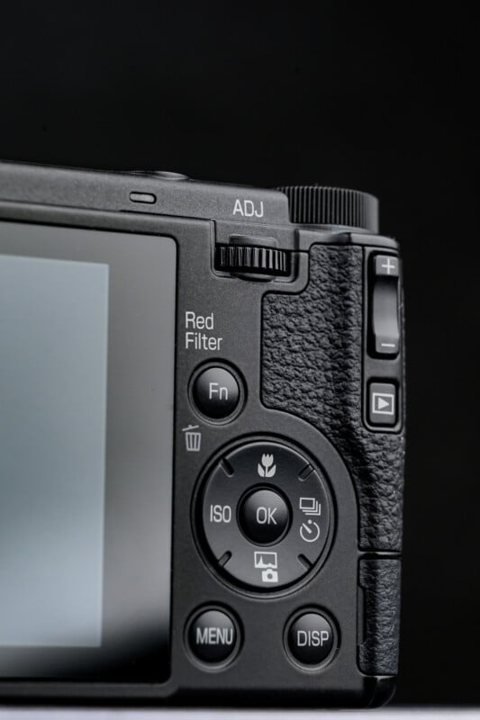 Close-up of the back of a digital camera showing buttons, dials, and part of the screen. Visible labels include "Red Filter," "Fn," "ISO," "MENU," "DISP," and an adjustment dial. The camera is black with a textured grip.