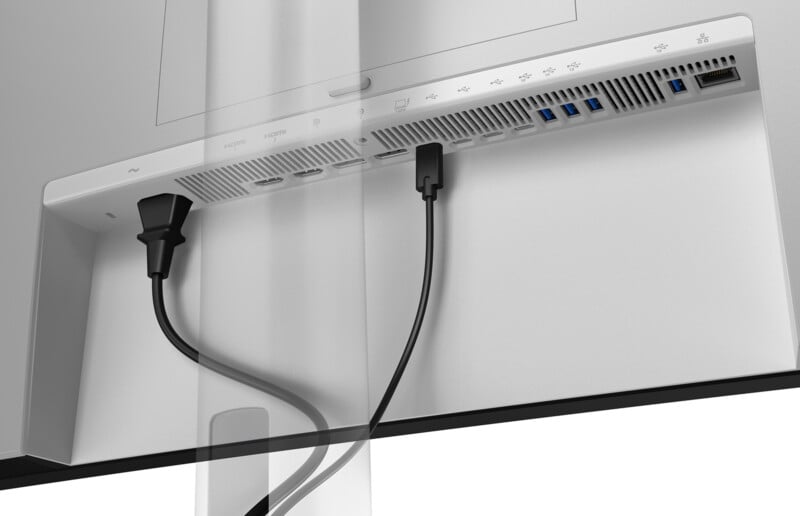The image shows the back panel of a computer monitor with two cables plugged into HDMI and DisplayPort slots, alongside USB, audio, and Ethernet ports. The monitor is mounted on a stand.