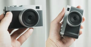 A hand holds a compact, modern camera with a prominent lens, photographed from two different angles against a neutral, blurred background.