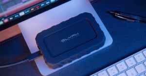 A rugged black Glyph external hard drive is connected to a laptop, sitting on a mouse pad next to a keyboard and a black pen.