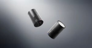 Two black cylindrical electronic devices with control buttons and vent slots are floating against a gradient gray background. One device shows its side and the other displays its bottom controls.