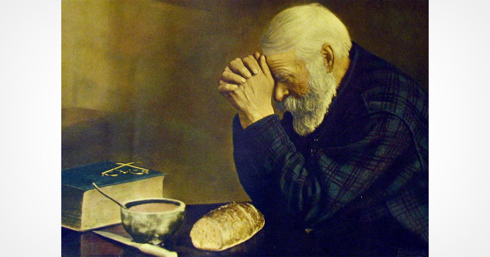 An elderly man with white hair and a beard sits at a table, hands clasped in prayer over a loaf of bread, a bowl, and a book, with his eyes closed in contemplation.