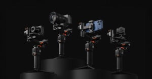 Four camera stabilizers, each holding a different device: a DSLR camera, a mirrorless camera, a smartphone, and an action camera, are displayed on black podiums against a dark background.