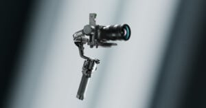 A professional camera mounted on a handheld gimbal stabilizer, floating against a softly lit, blurred background with light beams.