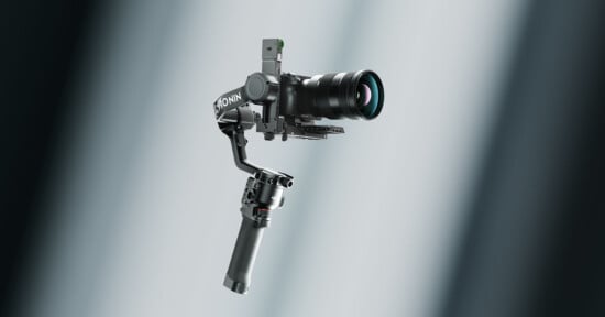 A professional camera mounted on a handheld gimbal stabilizer, floating against a softly lit, blurred background with light beams.