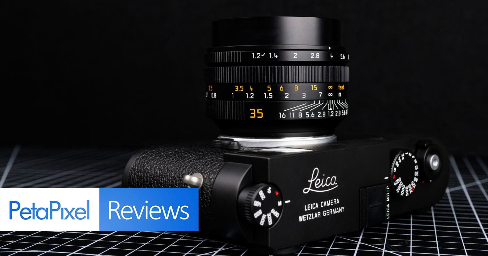 A Leica camera with a 35mm lens is placed on a black grid-patterned surface. The PetaPixel logo and the word "Reviews" appear in blue and white boxes in the bottom left corner.