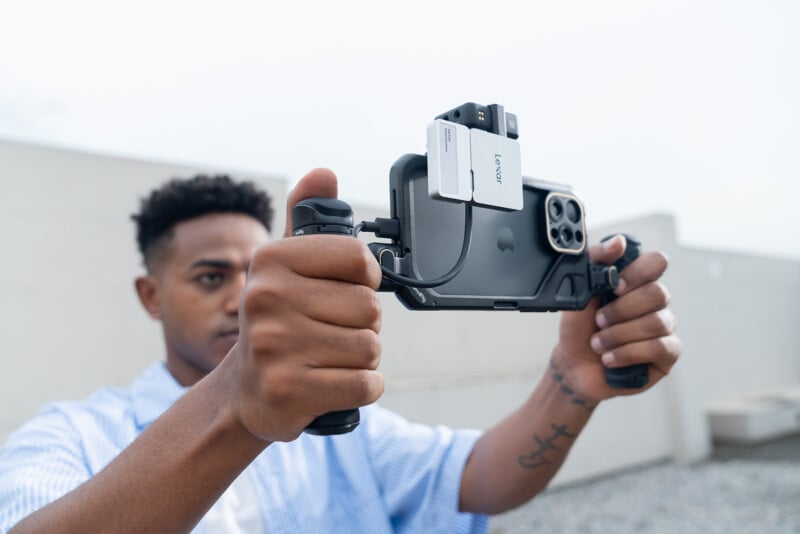A person holds a smartphone mounted in a stabilizing rig with attached accessories, focusing intently while preparing to record or take a photo outdoors.