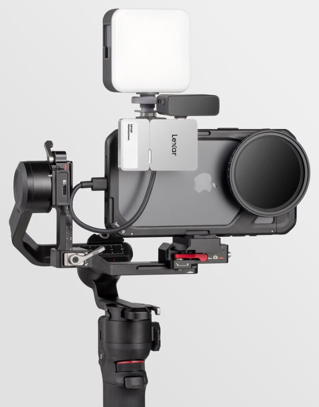 A smartphone mounted on a stabilizing gimbal rig with an attached lens filter, a Lexar memory card reader, a microphone, and an LED light, all set up for professional video recording.