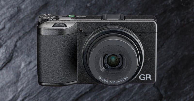 A compact black digital camera with a textured grip and a prominent lens, labeled "GR," is shown against a dark, stone-textured background.