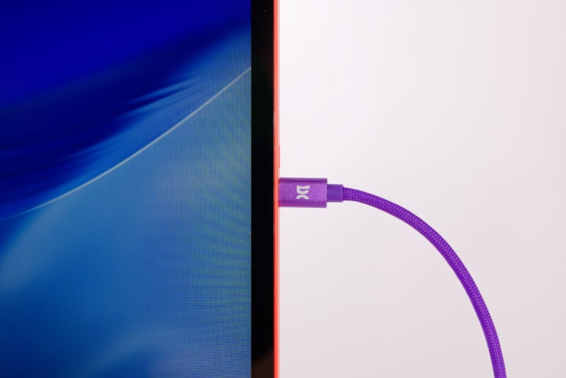 A close-up of a purple braided cable plugged into the side of a thin computer monitor with a blue screen, against a plain white background.