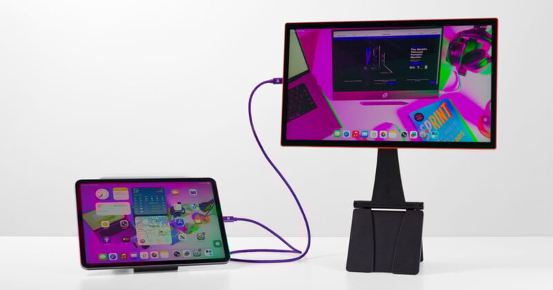 A tablet connected to a desktop monitor with a purple cable; both screens display similar digital content. The devices are on a white surface against a plain white background.