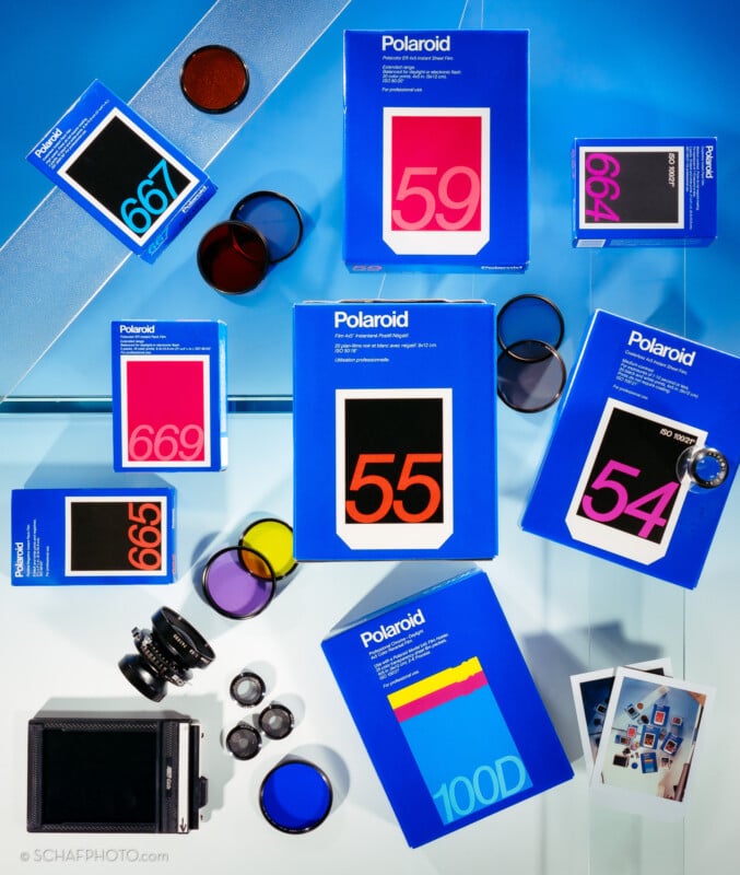 A flat lay of blue Polaroid film boxes with bold numbers, camera lenses, filters, an instant camera, and two Polaroid photos arranged on a blue and white background.