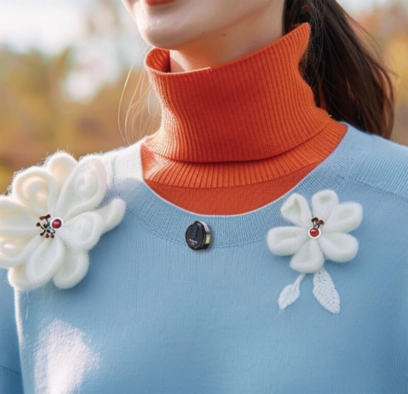 A woman wears an orange turtleneck under a light blue sweater, decorated with two large white flower-shaped brooches and a small round pin near the collar.