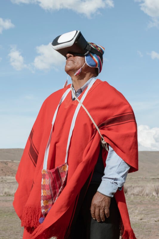 Un hombre vestido con ropa tradicional andina y un sombrero colorido usa un casco de realidad virtual al aire libre, de pie contra el fondo de un cielo brillante y un paisaje natural.
