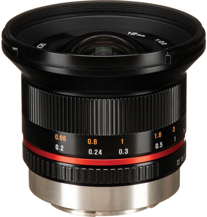 A wide-angle camera lens with a black body, ribbed focus ring, and red accent ring. White and orange distance markings are visible around the barrel. The lens cap is off, showing the front glass element.