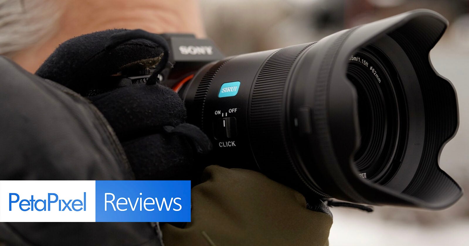 A close-up of a gloved person holding a Sony camera with a large lens. The image includes the "PetaPixel Reviews" logo in the bottom left corner.