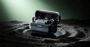 A black SmallRig wireless earbud case sits open on a textured, dark, crater-like surface, with the earbuds inside and subtle green lighting illuminating the background.