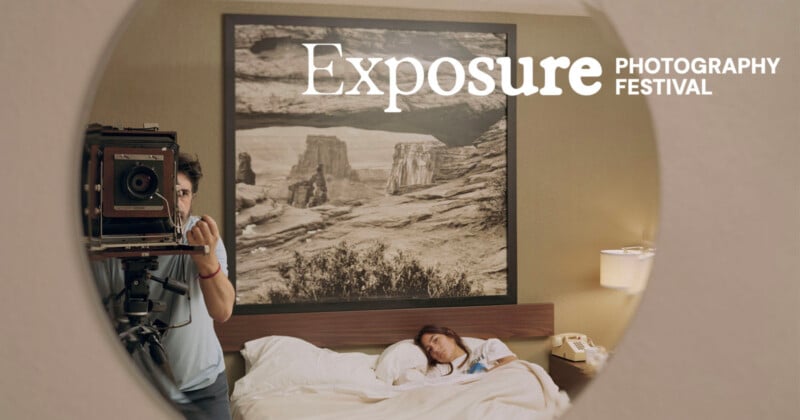 En la cama de una habitación de hotel, un hombre maneja una gran cámara de vídeo junto a una mujer acostada en la cama. Sobre la cama cuelga una fotografía de un paisaje. La escena se refleja en un espejo circular con el texto 