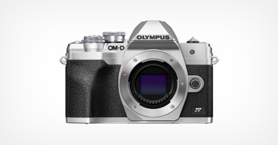 A silver and black Olympus OM-D digital camera body is shown facing forward on a plain white background, without a lens attached. The camera features textured grip and classic retro styling.
