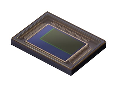 A close-up view of a digital image sensor chip, rectangular in shape with visible gold wire connections and a green-bordered central area, on a white background.
