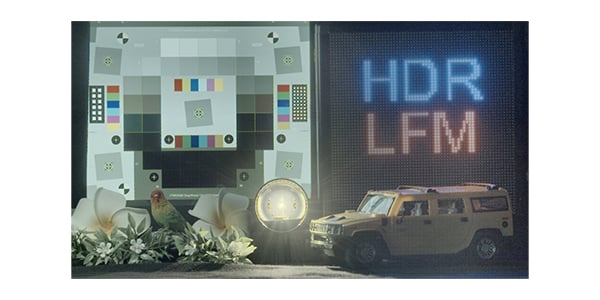 A scene with a test chart, illuminated coin, toy yellow Hummer car, artificial flowers, a bird figurine, and an LED display showing "HDR LFM" in blue and red text on the right side.