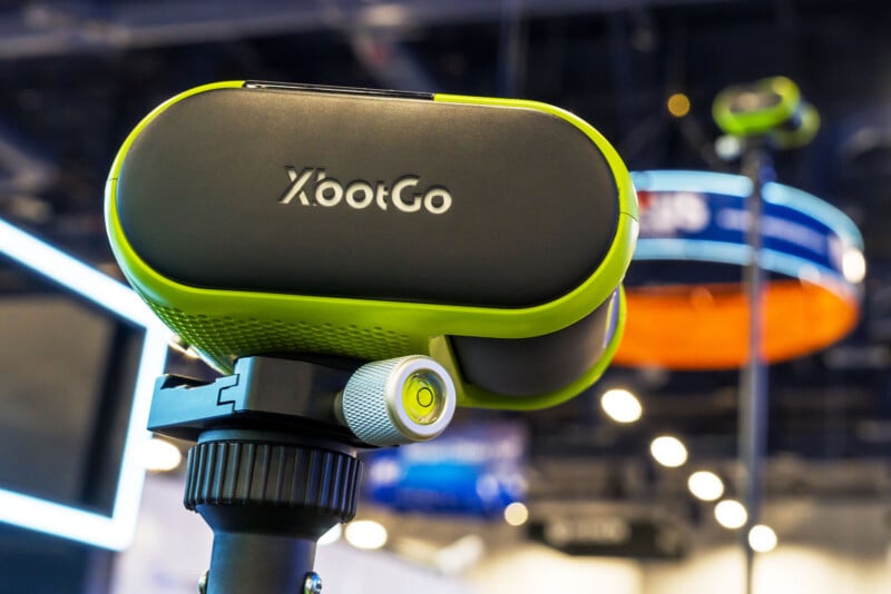 Primer plano del dispositivo XbootGo verde y negro montado en un trípode con fondo interior borroso con logotipo circular y luces.