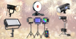 A variety of professional photography lights, including LED panels, ring light, and strobes, are arranged on a peach background with fireworks. Some lights are on stands, and a smartphone displays color controls.