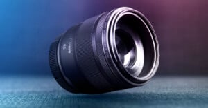 A close-up of a Canon 45mm camera lens resting on its side on a textured surface, with soft blue and purple lighting in the background.